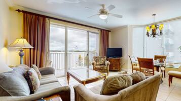A spacious living room with a sofa, armchairs, a glass coffee table, a television, and a dining area with a chandelier.