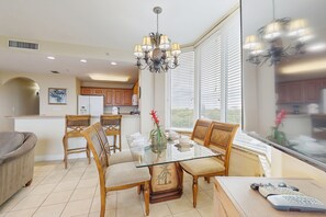 A dining area with a glass table, wooden chairs, a chandelier, and a view through large windows. - Blue Heron Beach I (Orlando)