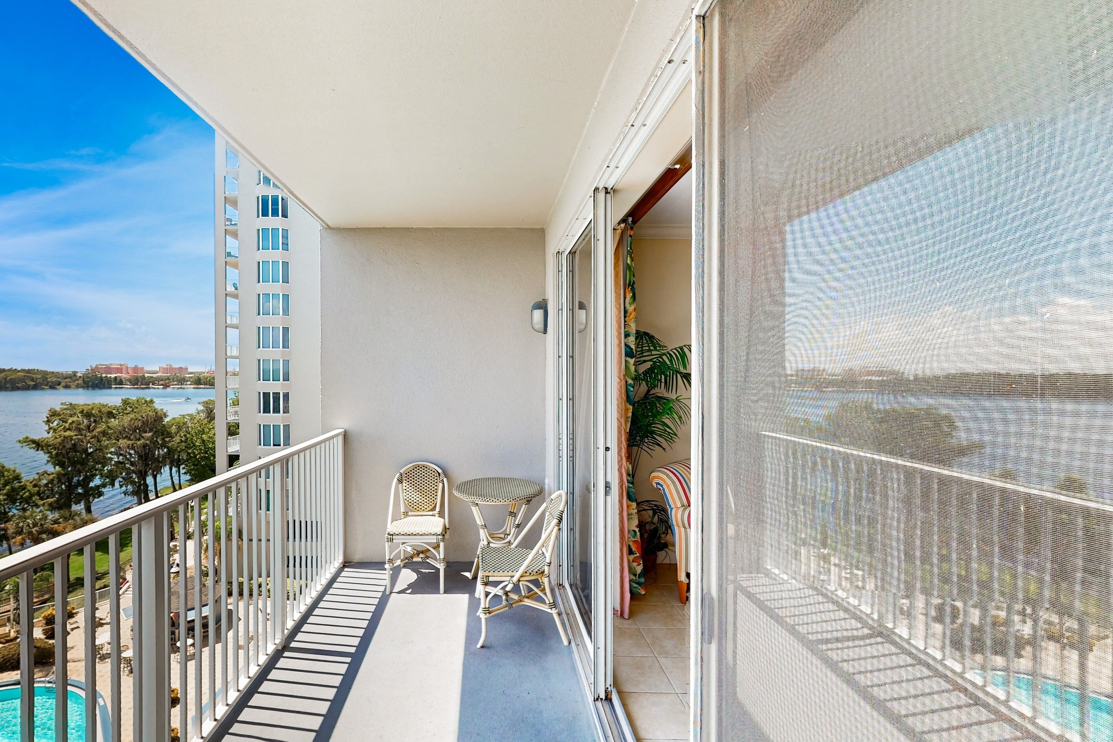 A balcony with a view of the sea, two wicker chairs, a small table, and a pool.