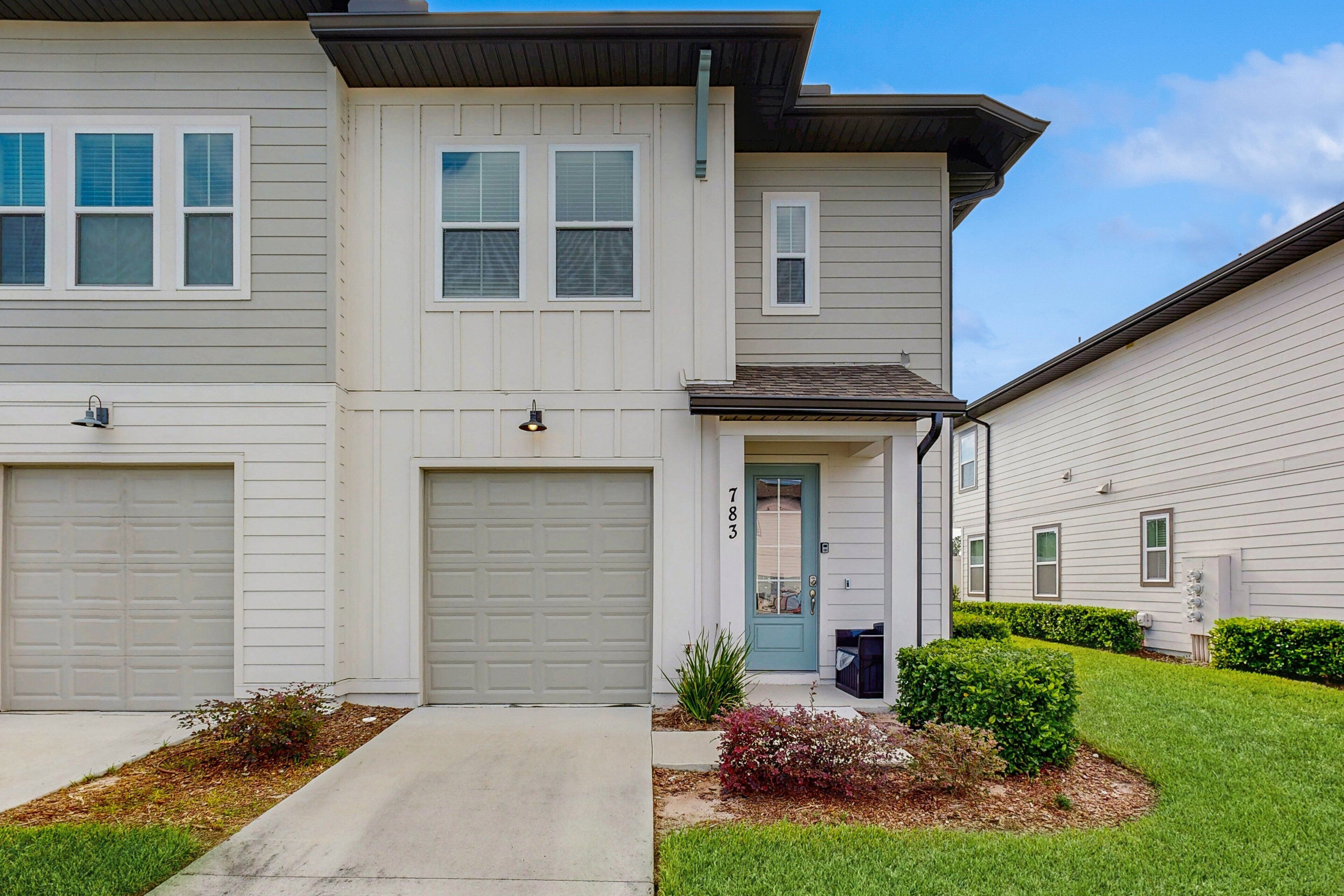 A two-story residential building with a garage, a front door, and a small front yard with landscaping.