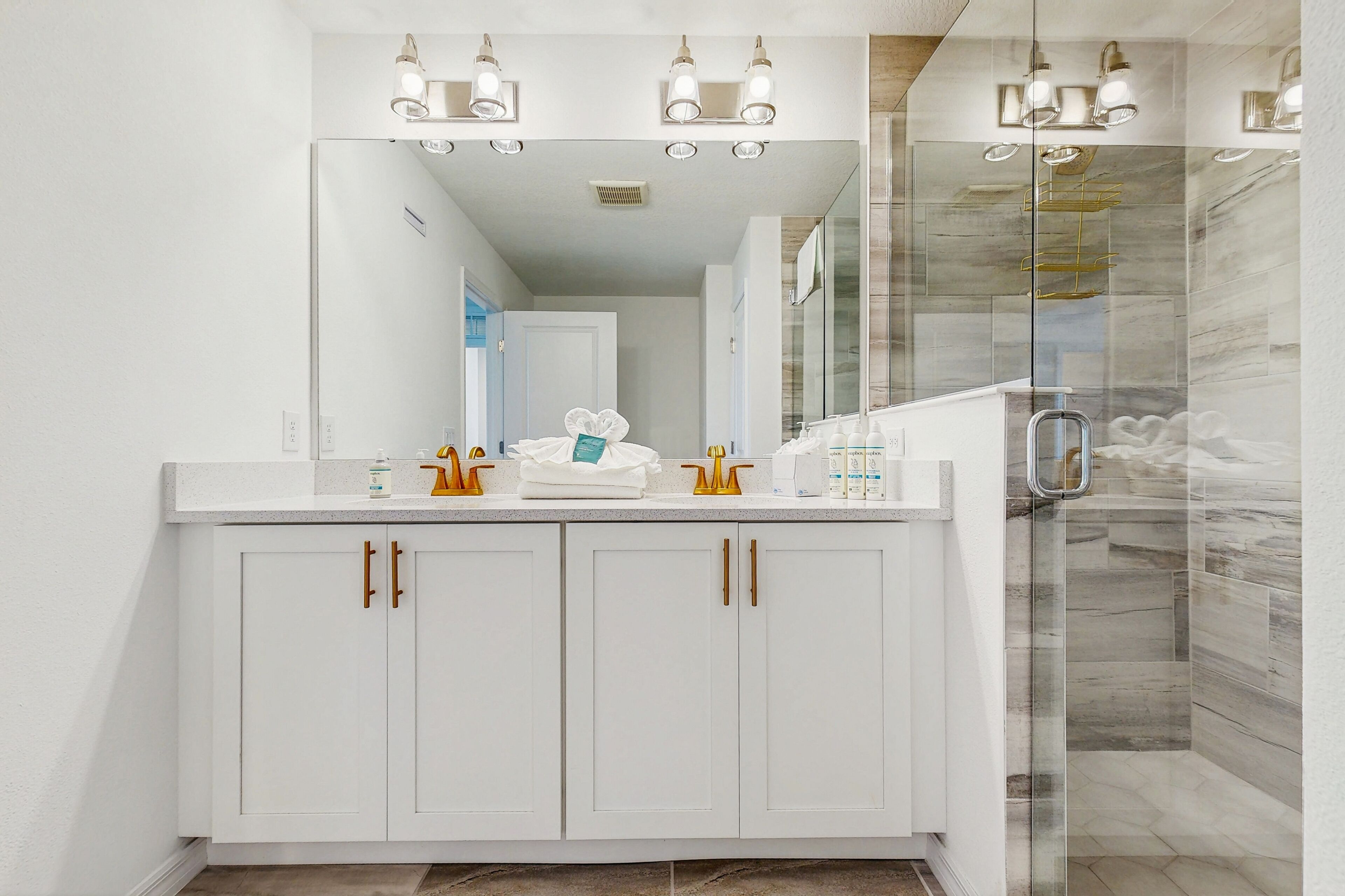 A modern bathroom with a white vanity, gold handles, and a glass shower enclosure.