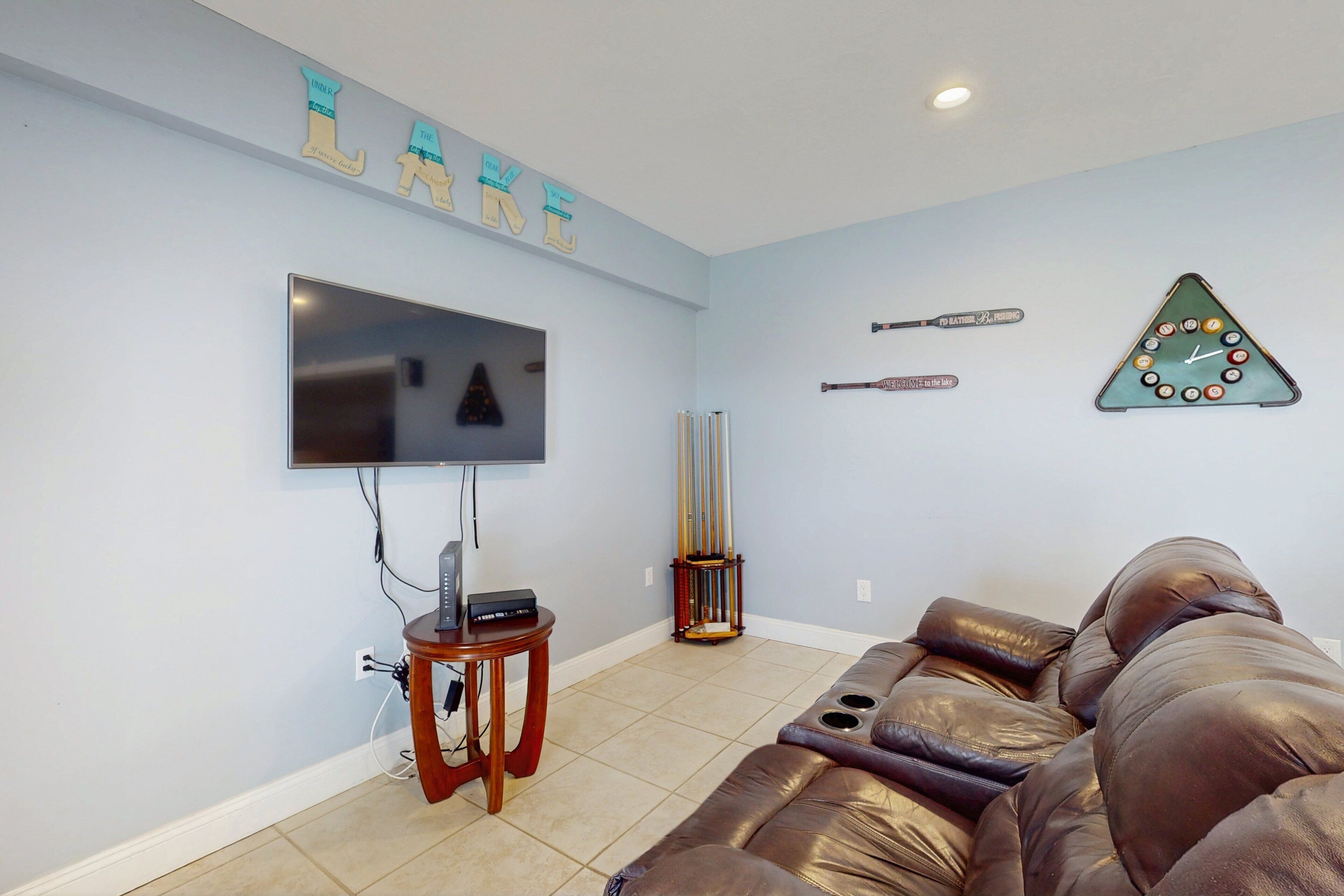 Una sala de estar con televisor, un sofá de cuero, un reloj y una pared decorada con recuerdos deportivos.