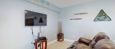 Una sala de estar con televisor, un sofá de cuero, un reloj y una pared decorada con recuerdos deportivos.