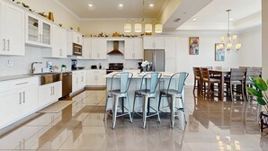 Una cocina moderna con armarios blancos, electrodomésticos de acero inoxidable y una isla central con taburetes de bar.