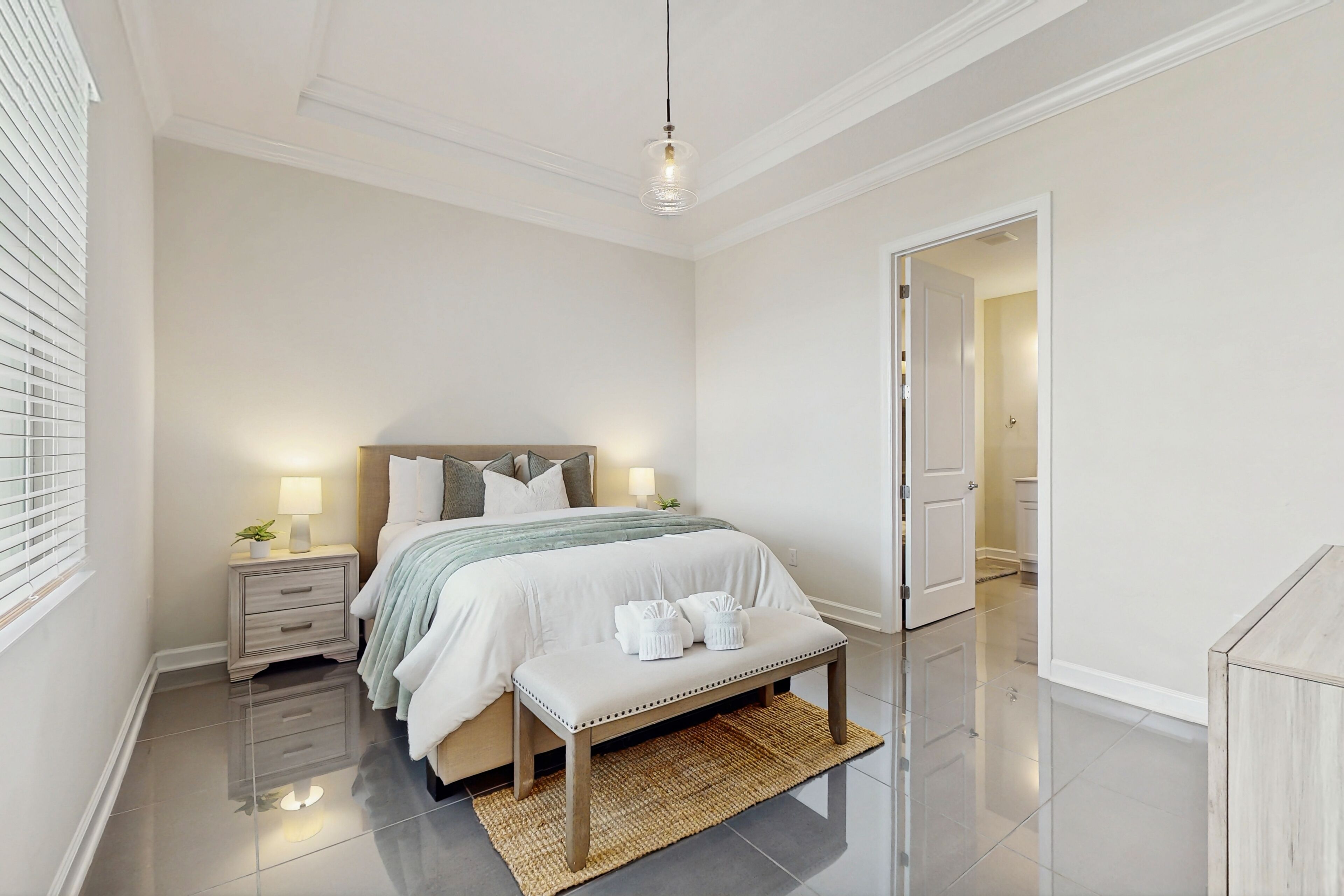 A bedroom with a bed, bedside tables, a bench, and a door leading to another room.