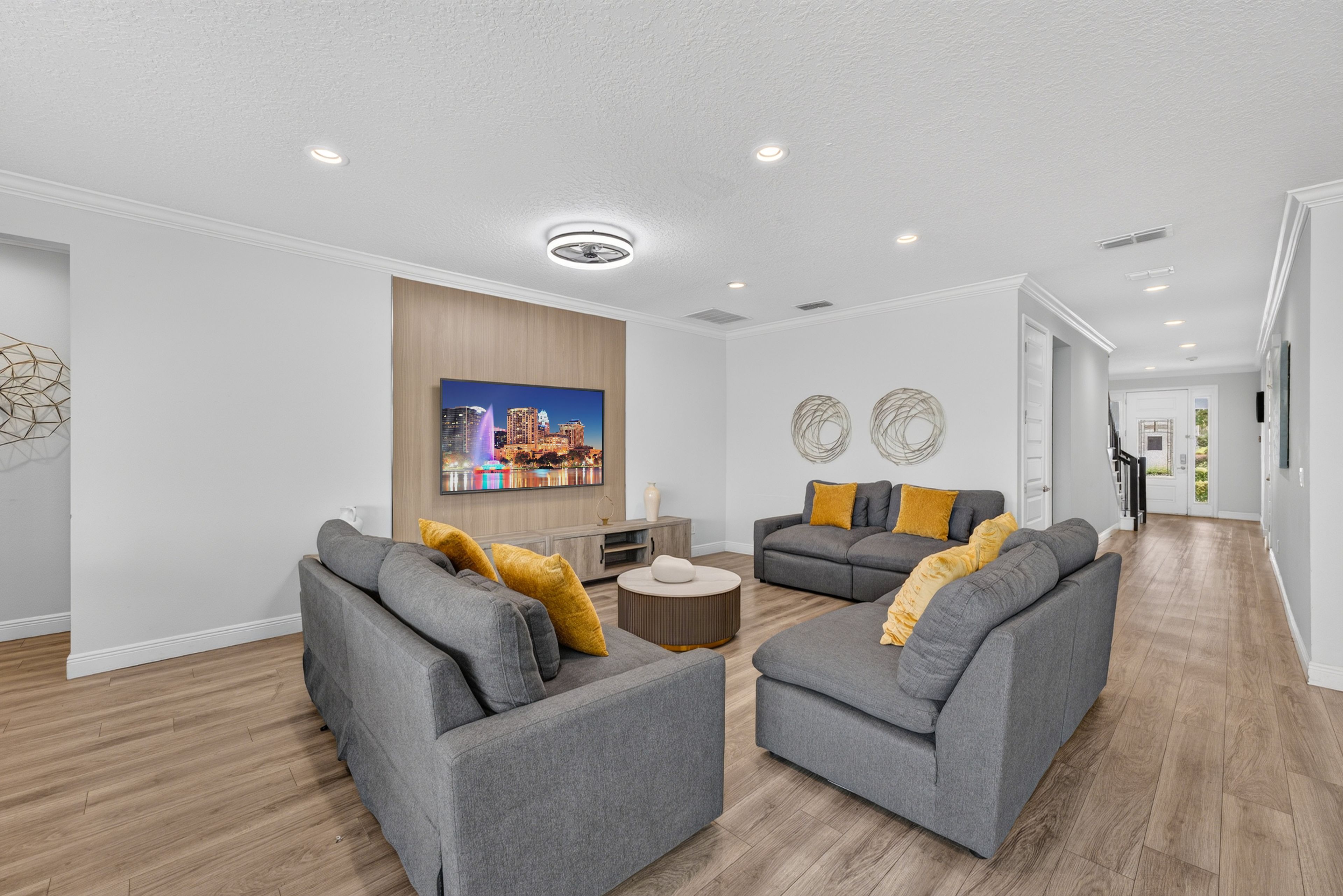 A modern living room with grey sofas, a coffee table, and a large flat-screen TV mounted on the wall.