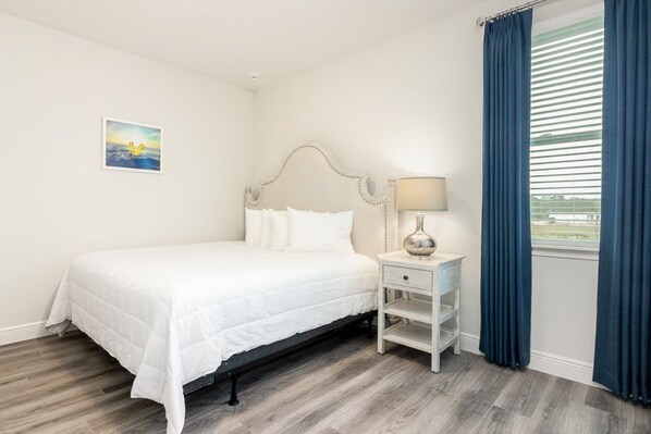 A bedroom with a bed, a nightstand, a lamp, a painting, and a window with curtains. - Luxurious Home Private Pool + Spa (Kissimmee)