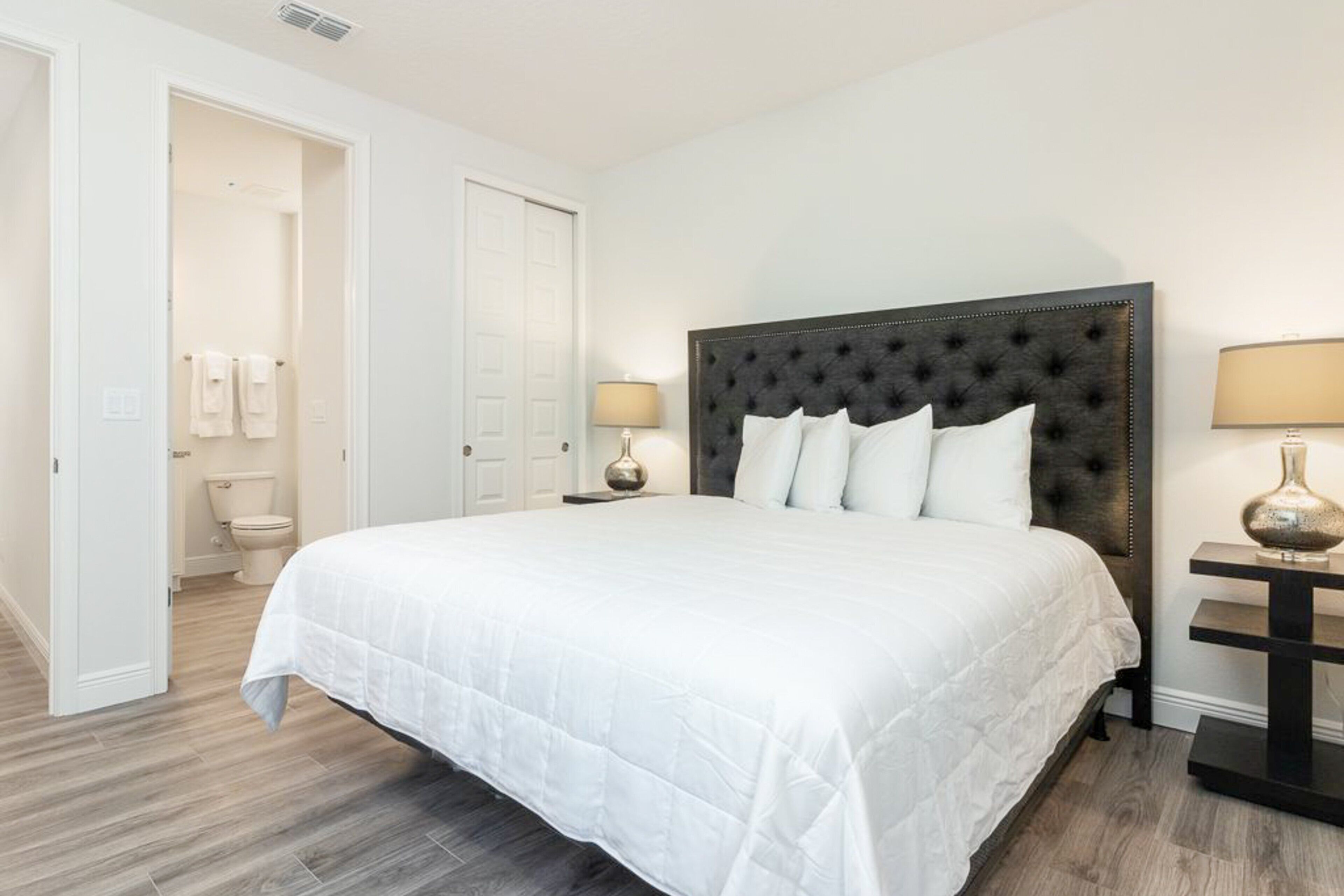 Une chambre à coucher avec un grand lit, une table de chevet avec une lampe et une porte donnant sur une salle de bain.