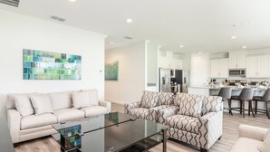 A modern living room with a glass coffee table, a beige sofa, and patterned armchairs. - Luxurious Home Private Pool + Spa (Kissimmee)