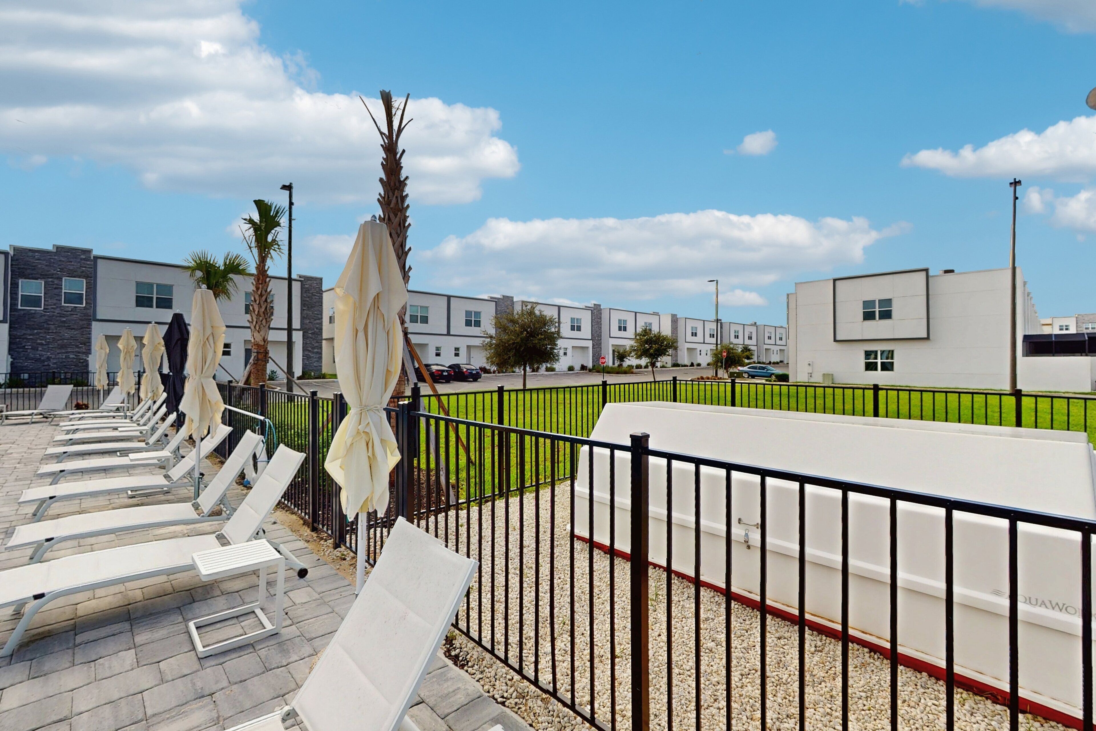 A row of sun loungers with umbrellas, a white fence, and modern buildings in the background.
