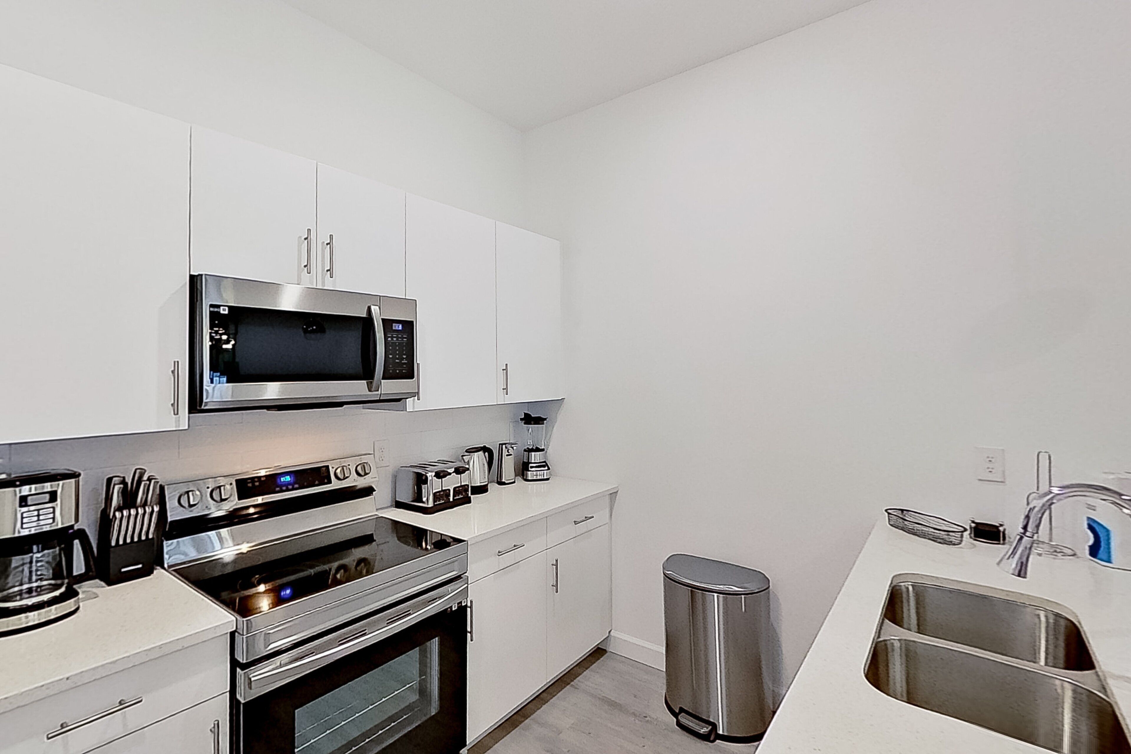 Una cocina moderna con electrodomésticos de acero inoxidable, armarios blancos y un fregadero.