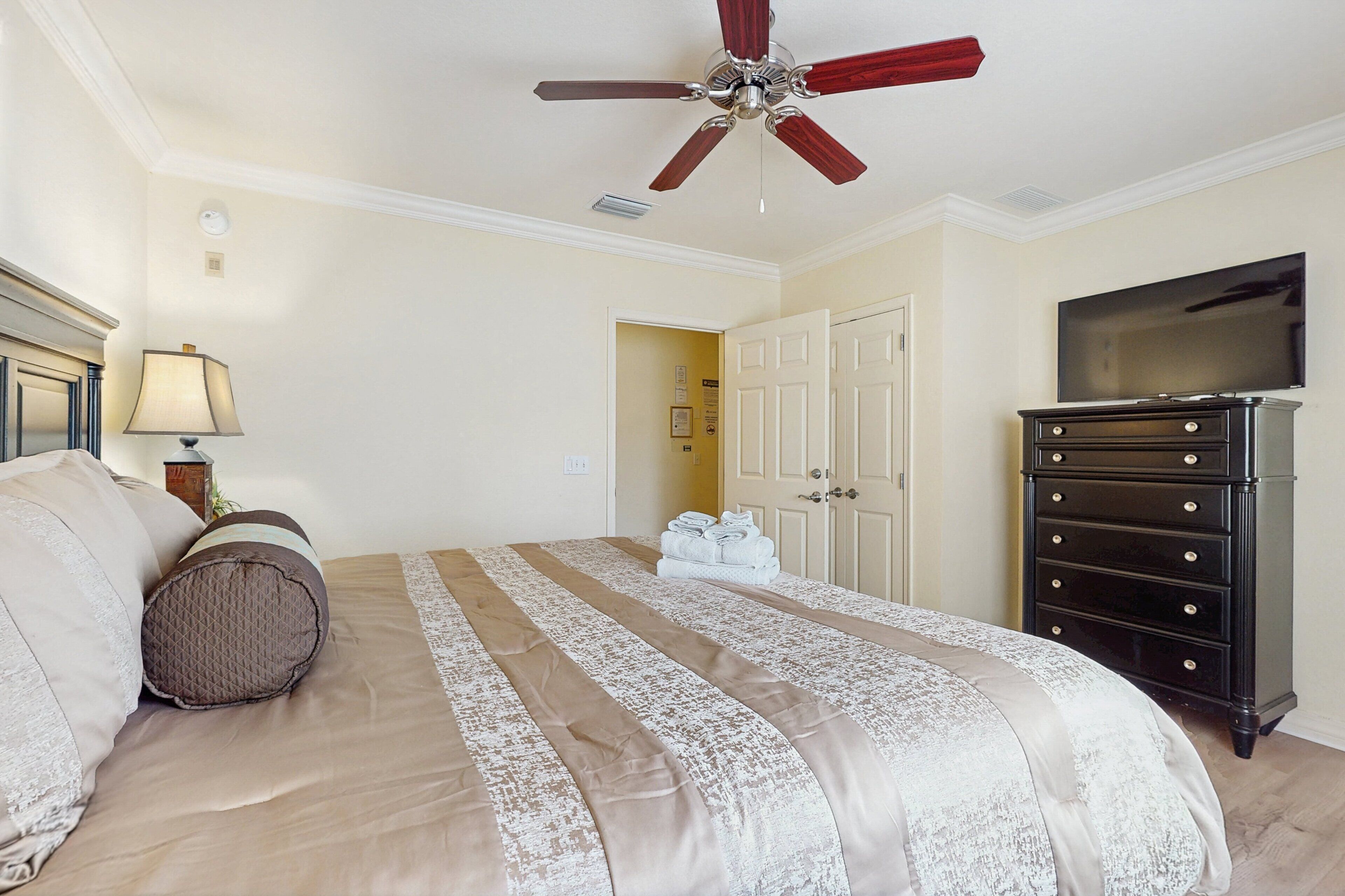 A hotel room with a bed, a ceiling fan, a dresser, and a television.