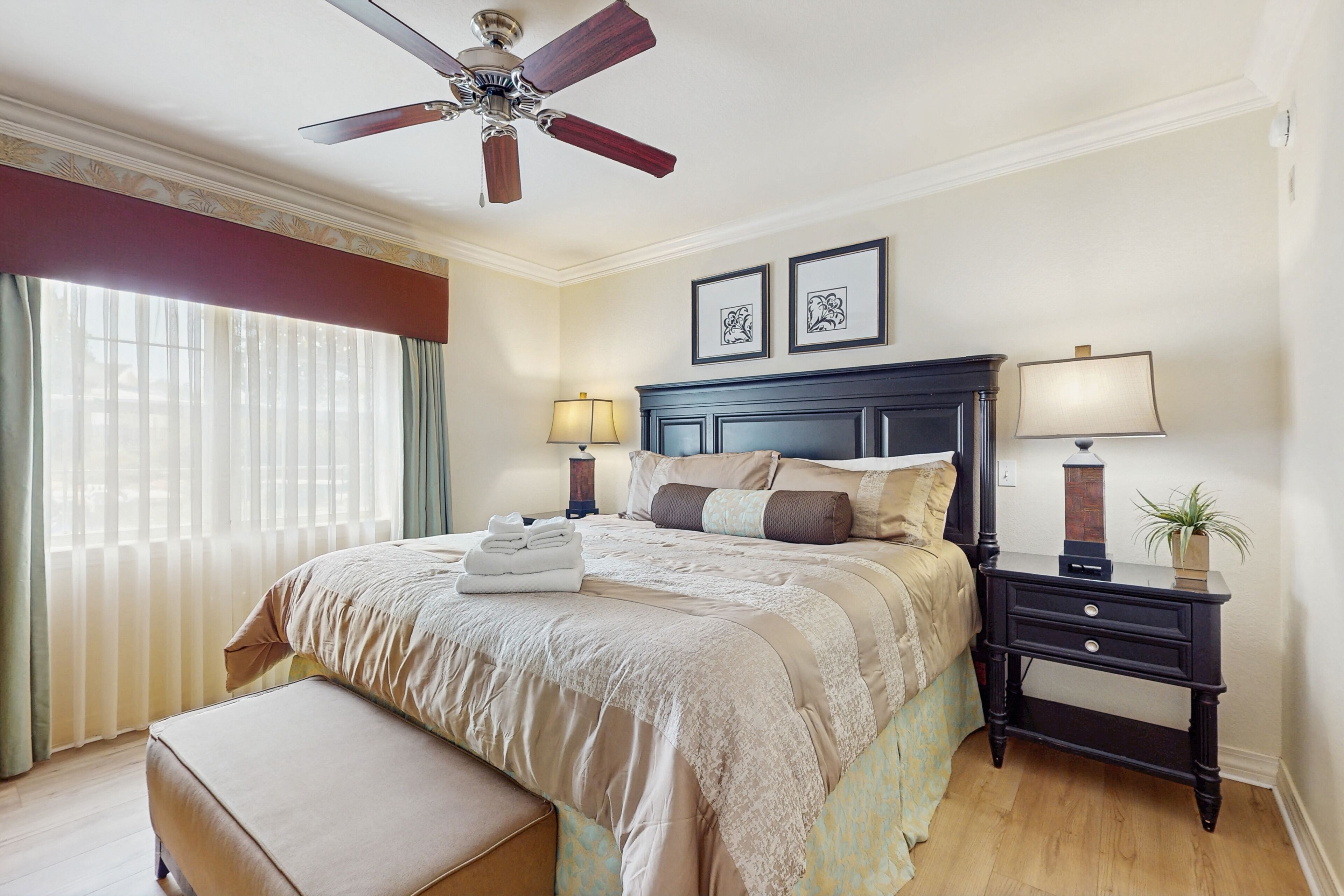 Une chambre bien rangée, avec un lit, des tables de chevet, un ventilateur de plafond et une fenêtre avec des rideaux.