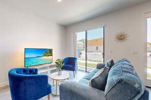 Una sala de estar moderna con un televisor de pantalla plana, un sillón azul, un sofá y una mesita con una planta.