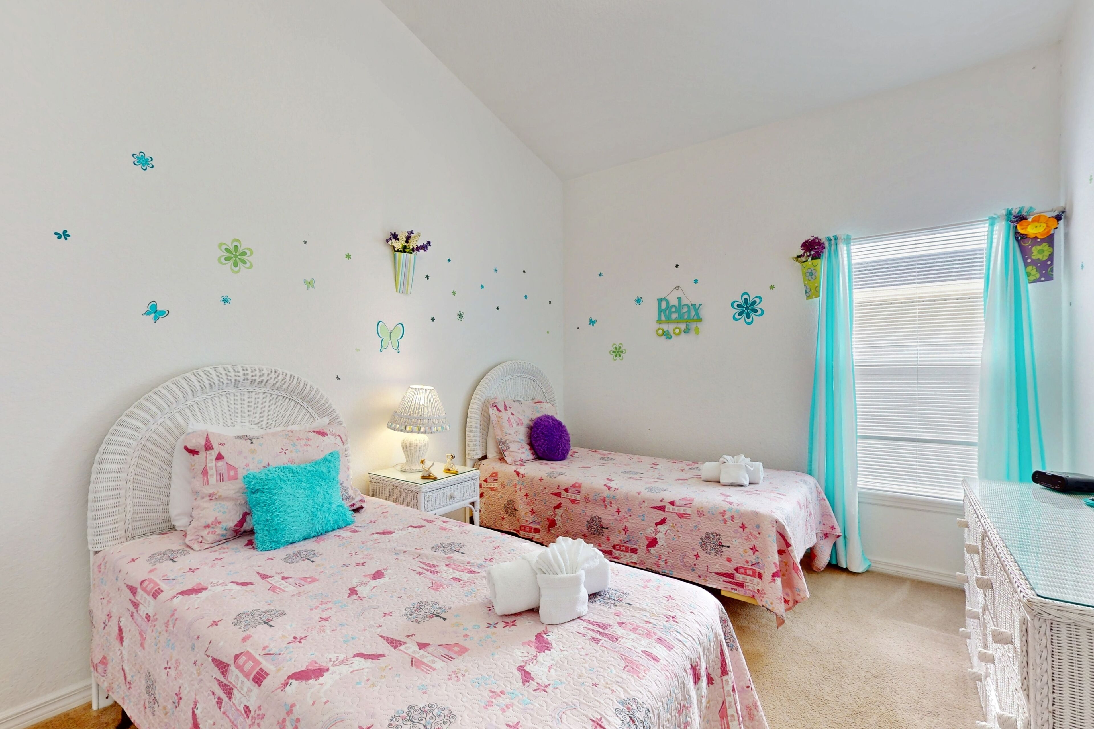 Une chambre à coucher avec deux lits, chacun recouvert d’une couvre-lit rose, doté d’une tête de lit blanche et agrémenté d’une petite table de chevet avec une lampe.