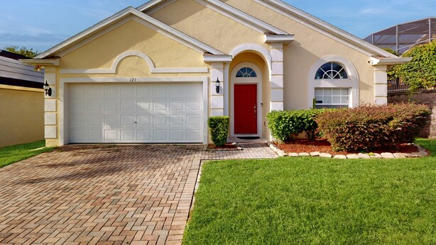 A two-story house with a red door, a garage, and a well-maintained lawn. - Spacious, Dog-friendly Home With Private Pool, Wifi, & Fun-filled Game Room (Davenport)