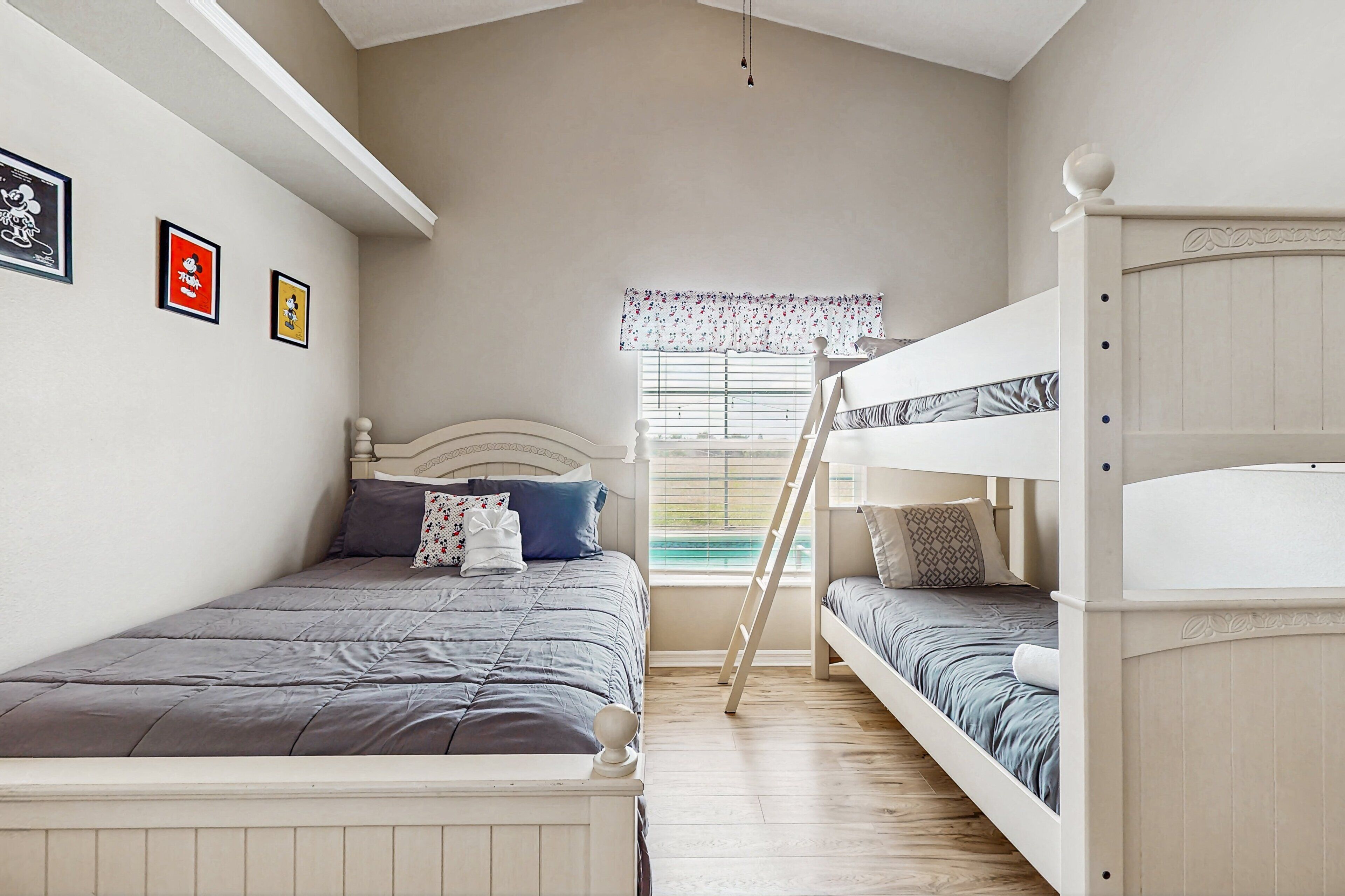 A bedroom with bunk beds, a window with blinds, and framed pictures on the wall.