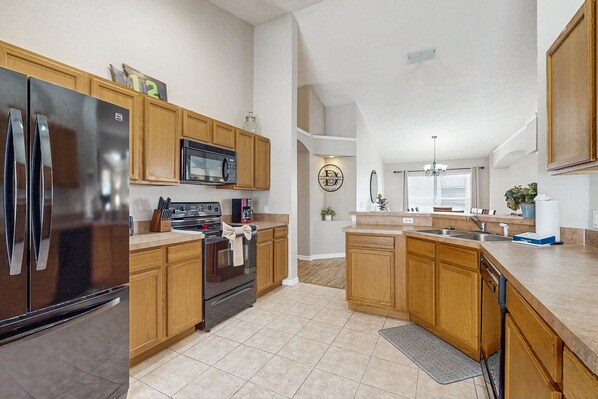 A modern kitchen with wooden cabinets, stainless steel appliances, and a central island. - Big & Beautiful Home Close to Theme Parks W/fast Wifi, Private Patio & Pool + AC (Davenport)