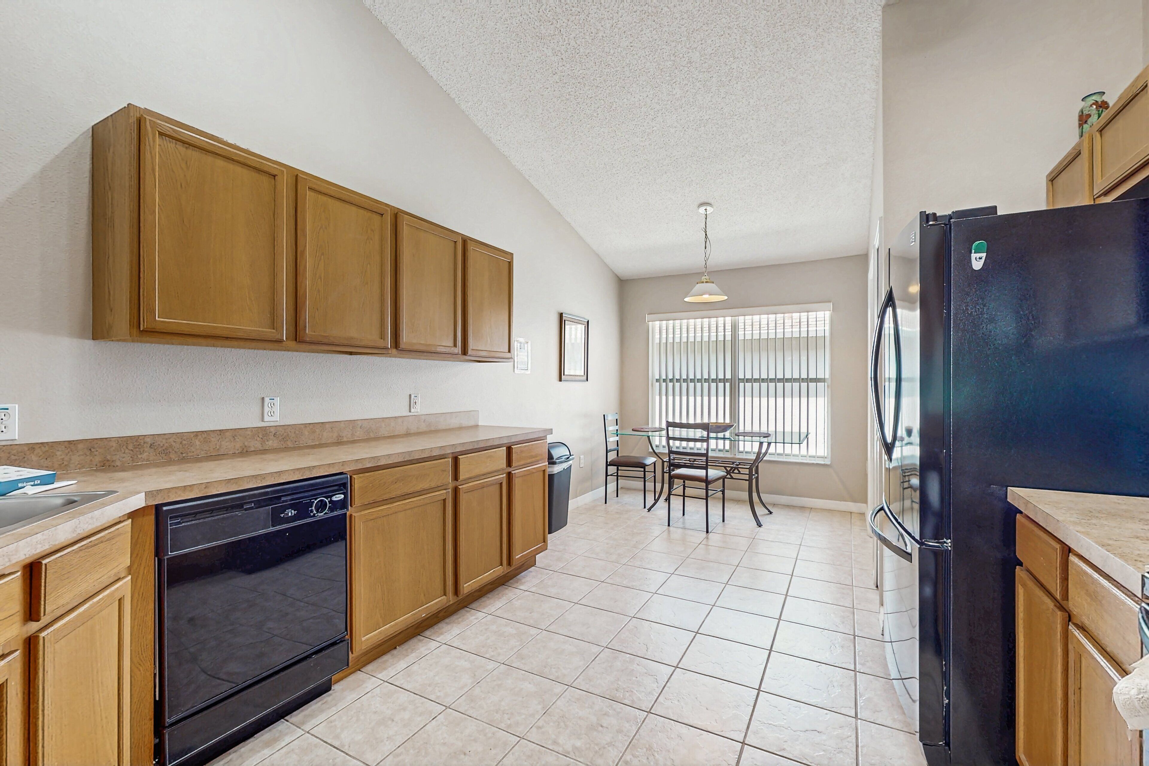 A kitchen with wooden cabinets, a dishwasher, a refrigerator, and a dining area with a table and chairs.