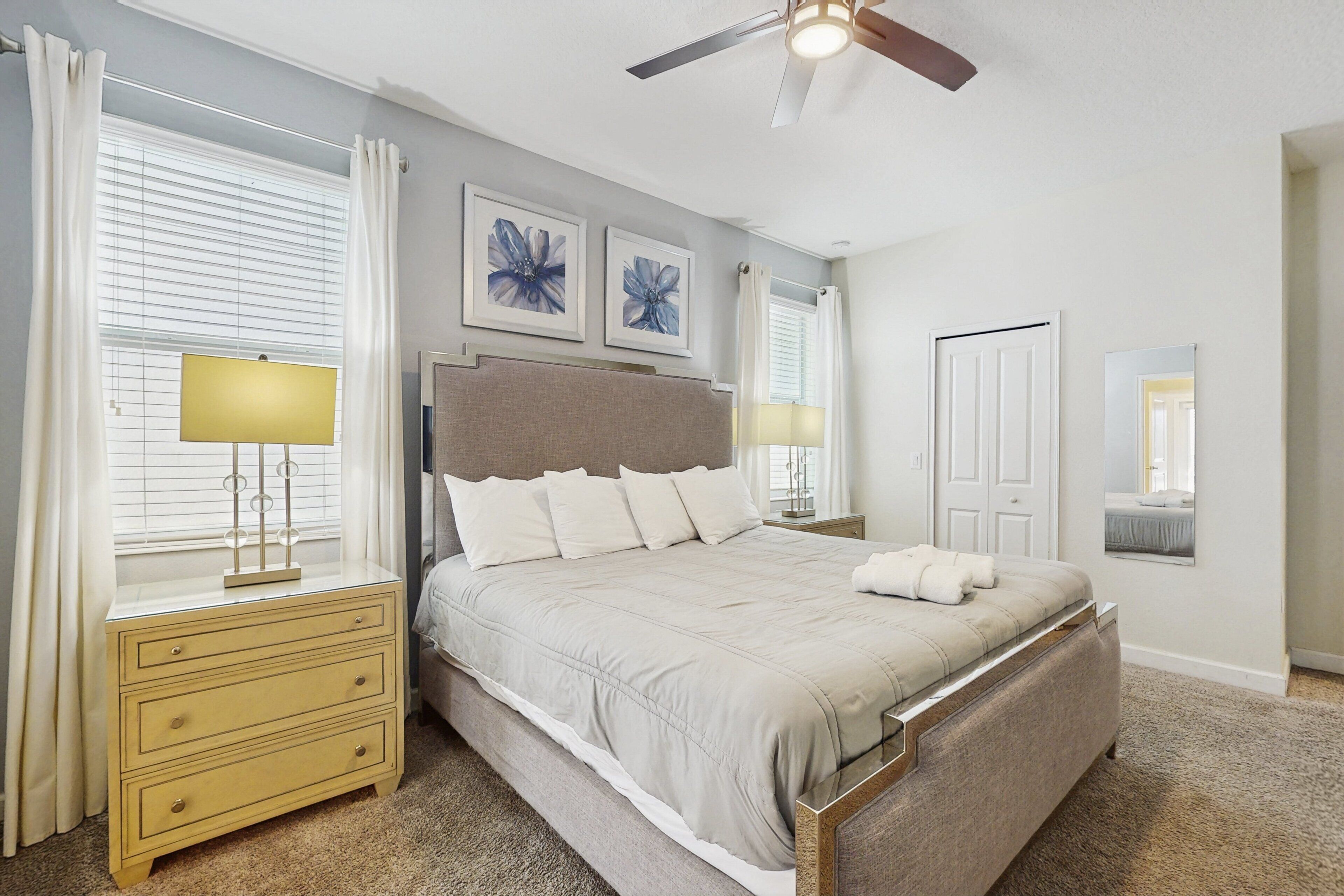 A bedroom with a bed, bedside tables, a ceiling fan, and artwork on the wall.