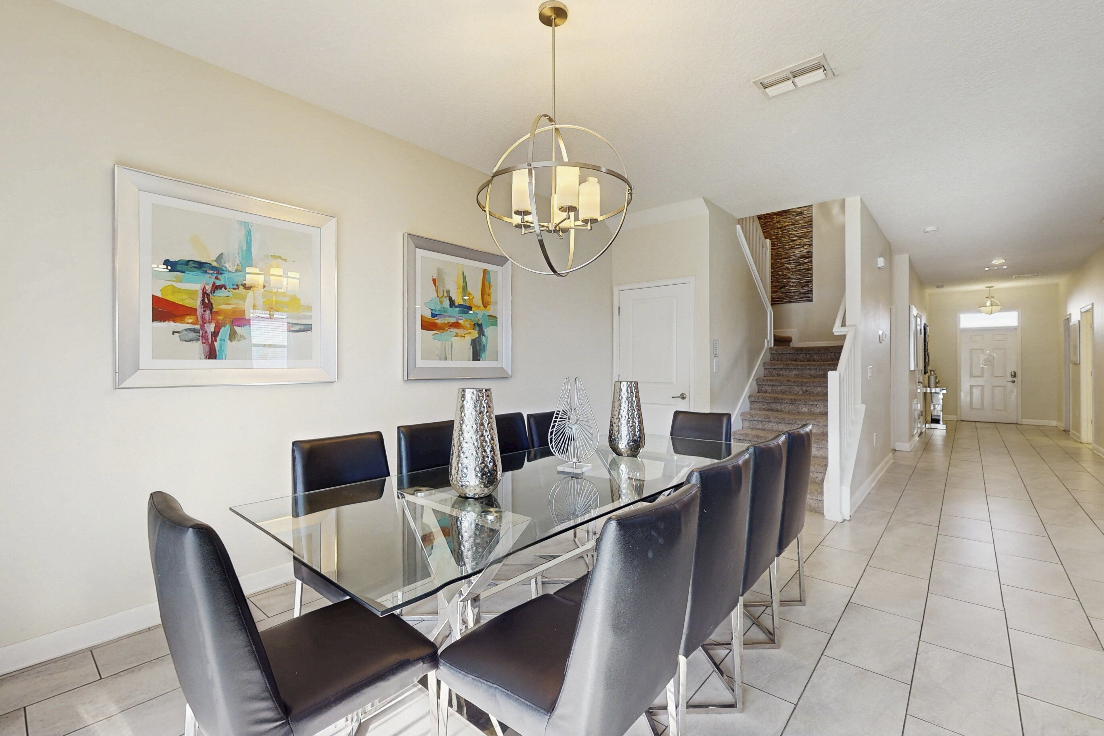 Un coin repas avec une table en verre, des chaises noires et deux tableaux abstraits accrochés au mur.