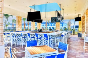 Eine Bar mit weißen und blauen Stühlen, einer langen Theke und mehreren Bildschirmen.