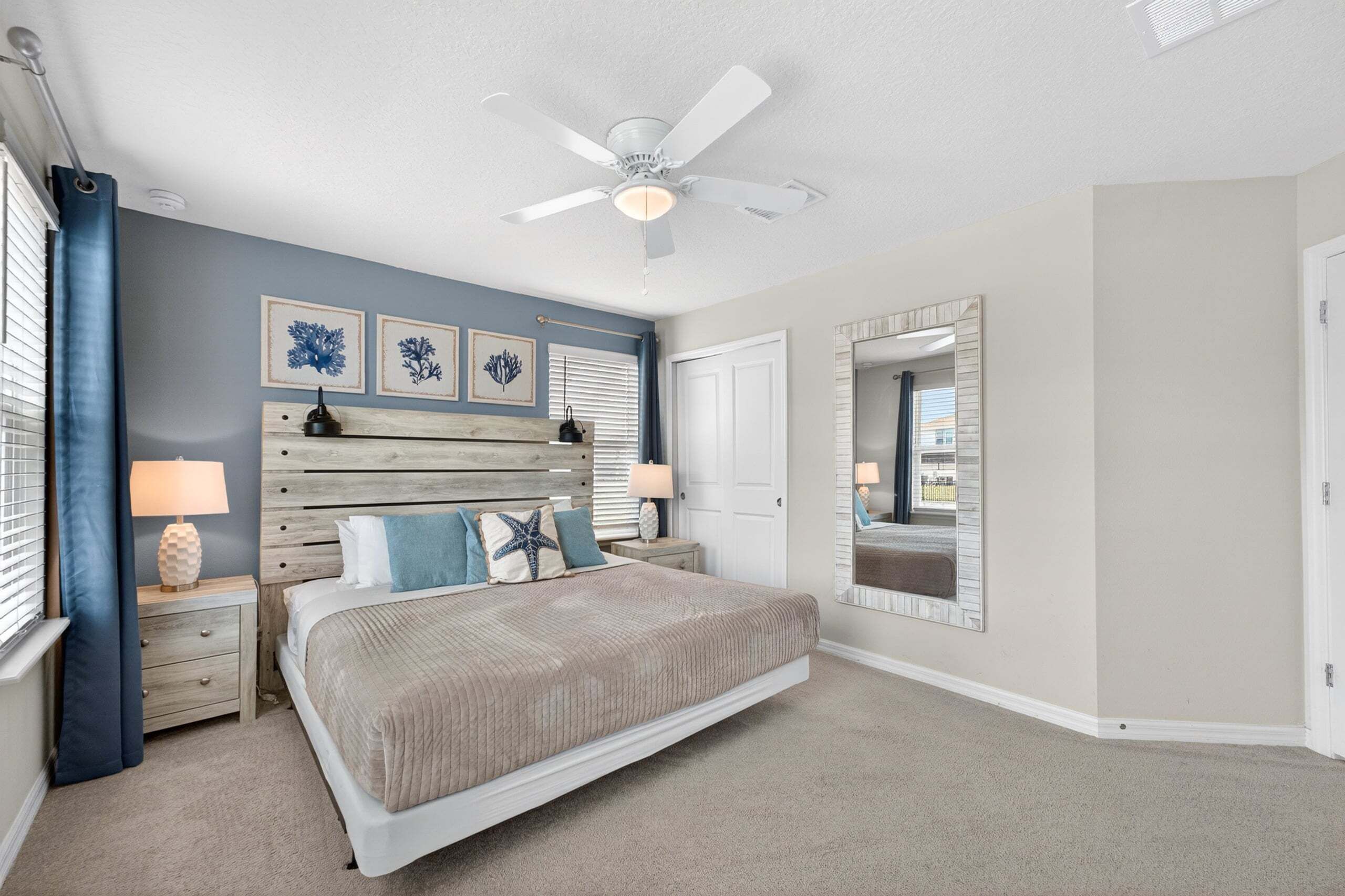 A bedroom with a bed, nightstands, a ceiling fan, wall art, and a mirror.
