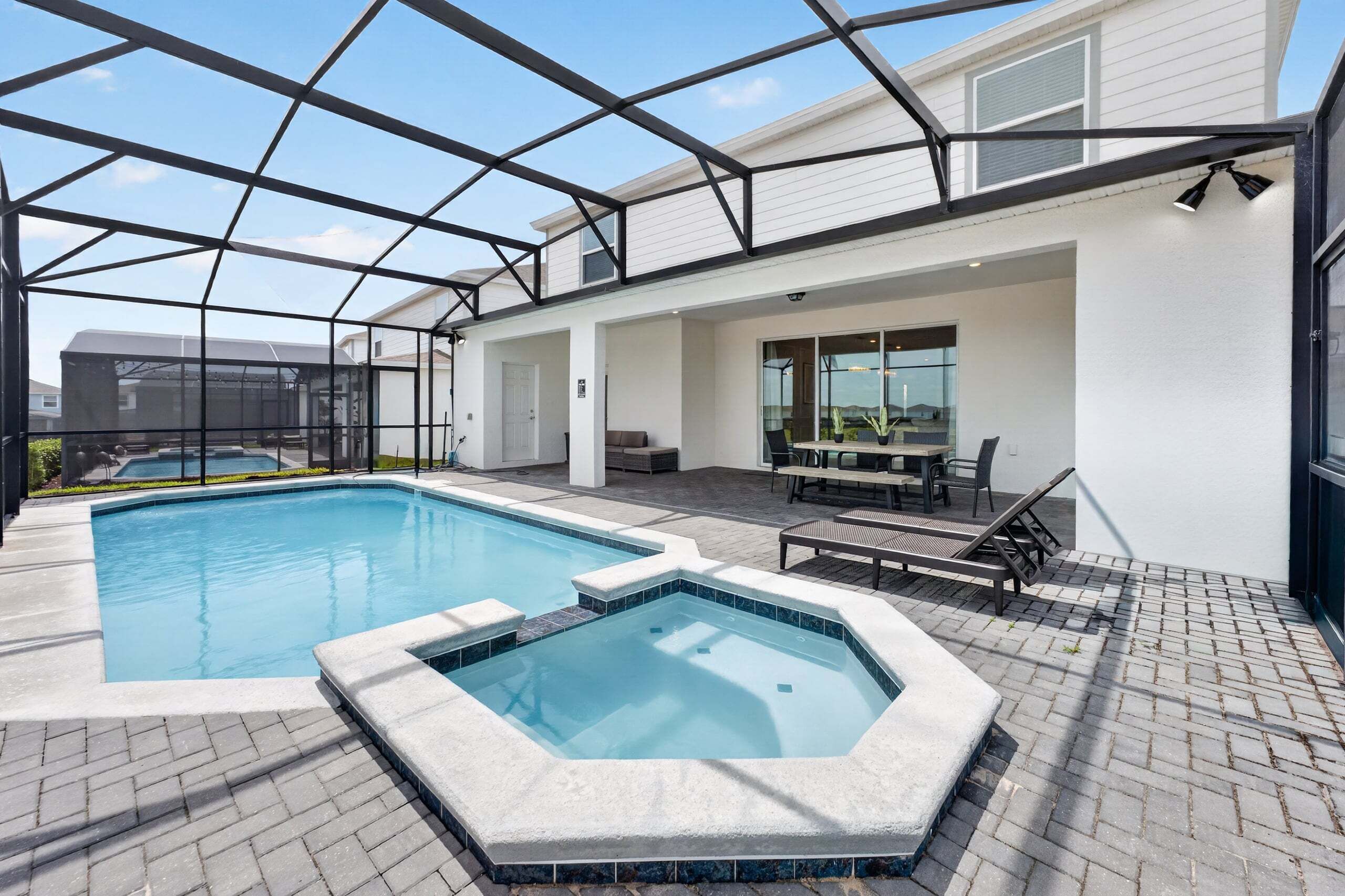 Una piscina con hidromasaje, mobiliario de exterior y un patio cubierto.
