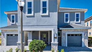 A two-story house with a garage, a front porch, and a well-maintained lawn. - Stunning Home With Private Pool/pool Spa, Golf Course View, & Home Theater (Kissimmee)