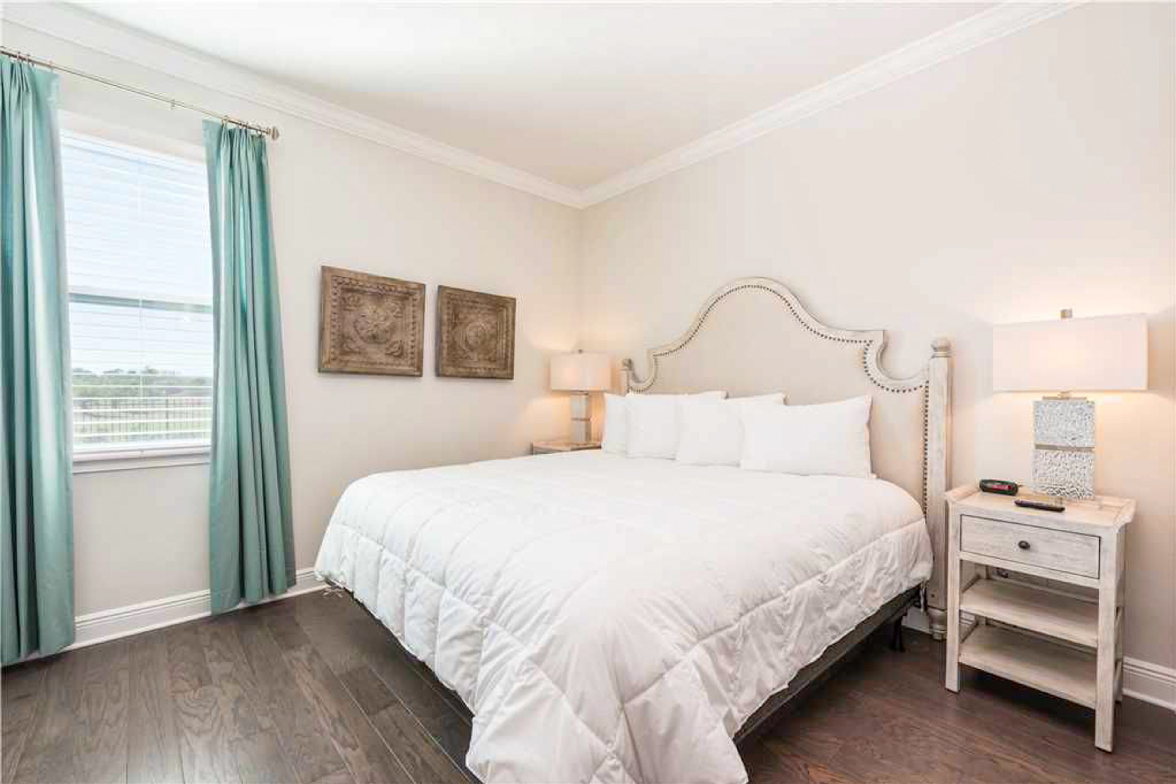 A neatly arranged bedroom with a large bed, a bedside table, and a window with curtains.