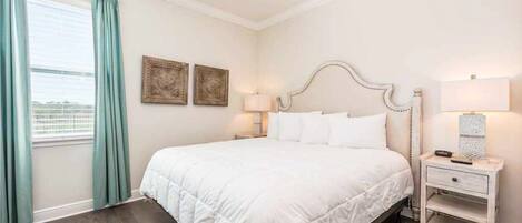 A neatly arranged bedroom with a large bed, a bedside table, and a window with curtains.