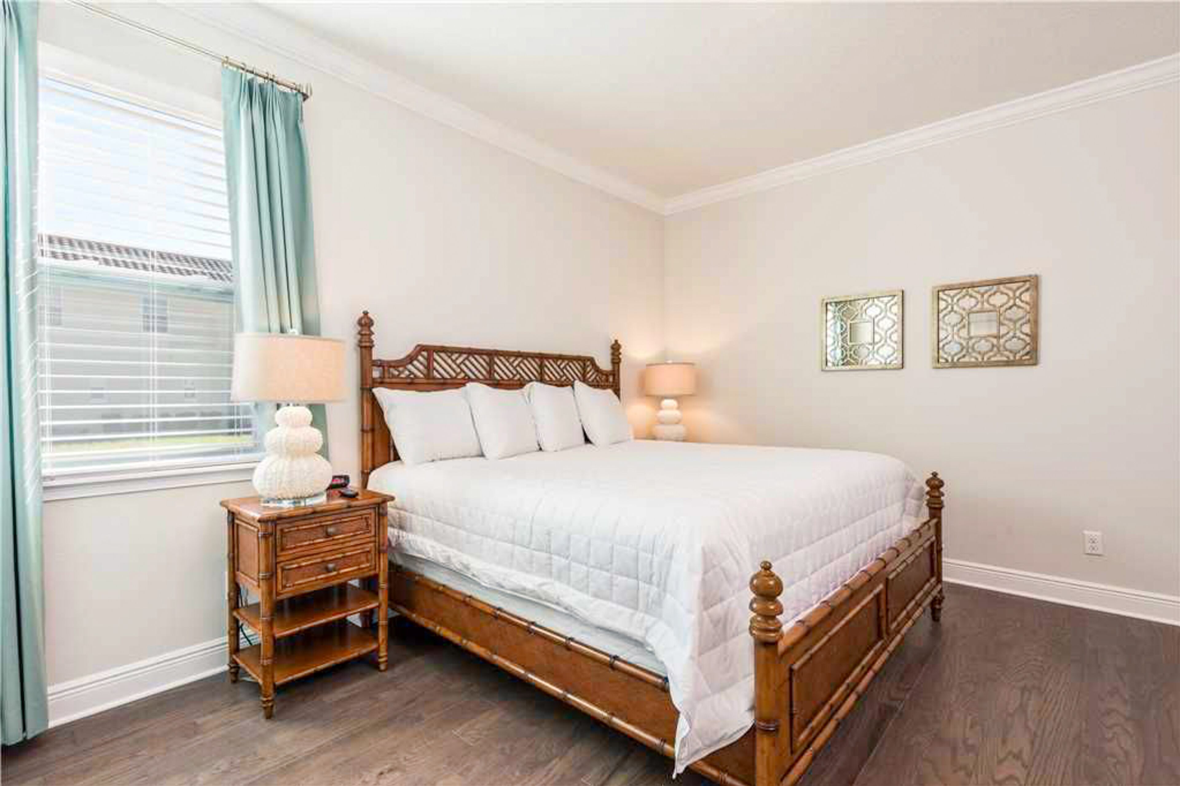 A bedroom with a wooden bed, two bedside lamps, a nightstand, and a window with curtains.