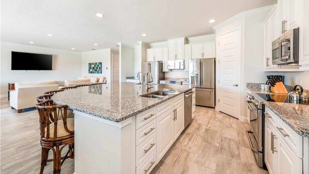 A modern kitchen with white cabinets, granite countertops, and stainless steel appliances. - Stunning Home With Private Pool/pool Spa, Golf Course View, & Home Theater (Kissimmee)