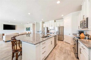 A modern kitchen with white cabinets, granite countertops, stainless steel appliances, and a bar area. - Stunning Home With Private Pool/pool Spa, Golf Course View, & Home Theater (Kissimmee)