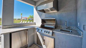 A modern outdoor kitchen with a built-in grill, a sink, and a view of a residential area. - Stunning Home With Private Pool/pool Spa, Golf Course View, & Home Theater (Kissimmee)