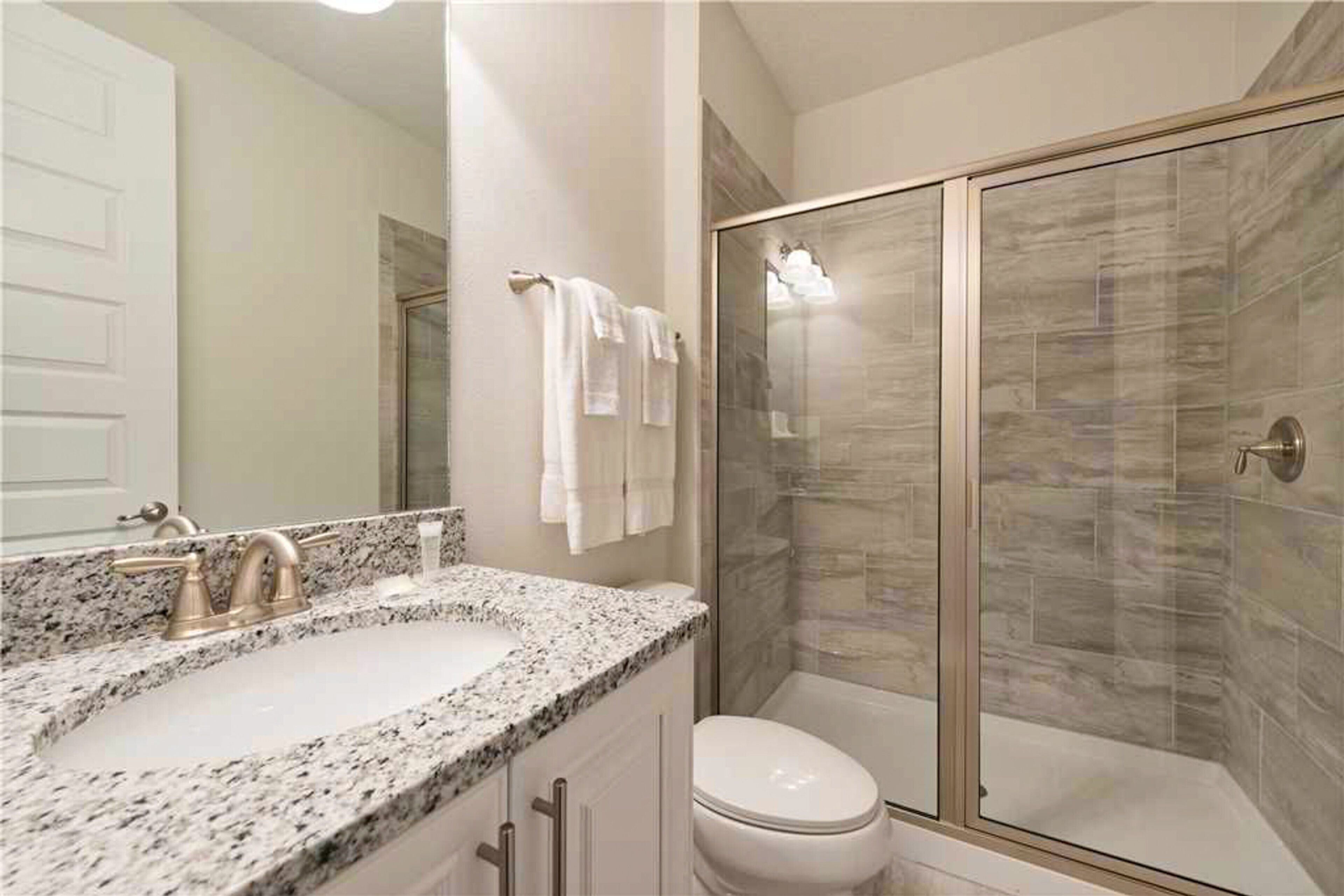 A bathroom with a granite countertop sink, a toilet, and a glass shower enclosure.