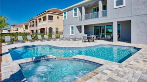 A swimming pool with lounge chairs, a hot tub, and a patio area with a table and chairs. - Stunning Home With Private Pool/pool Spa, Golf Course View, & Home Theater (Kissimmee)