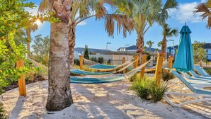 Un'area sulla spiaggia con sabbia, amache, palme e poltrone prendisole.