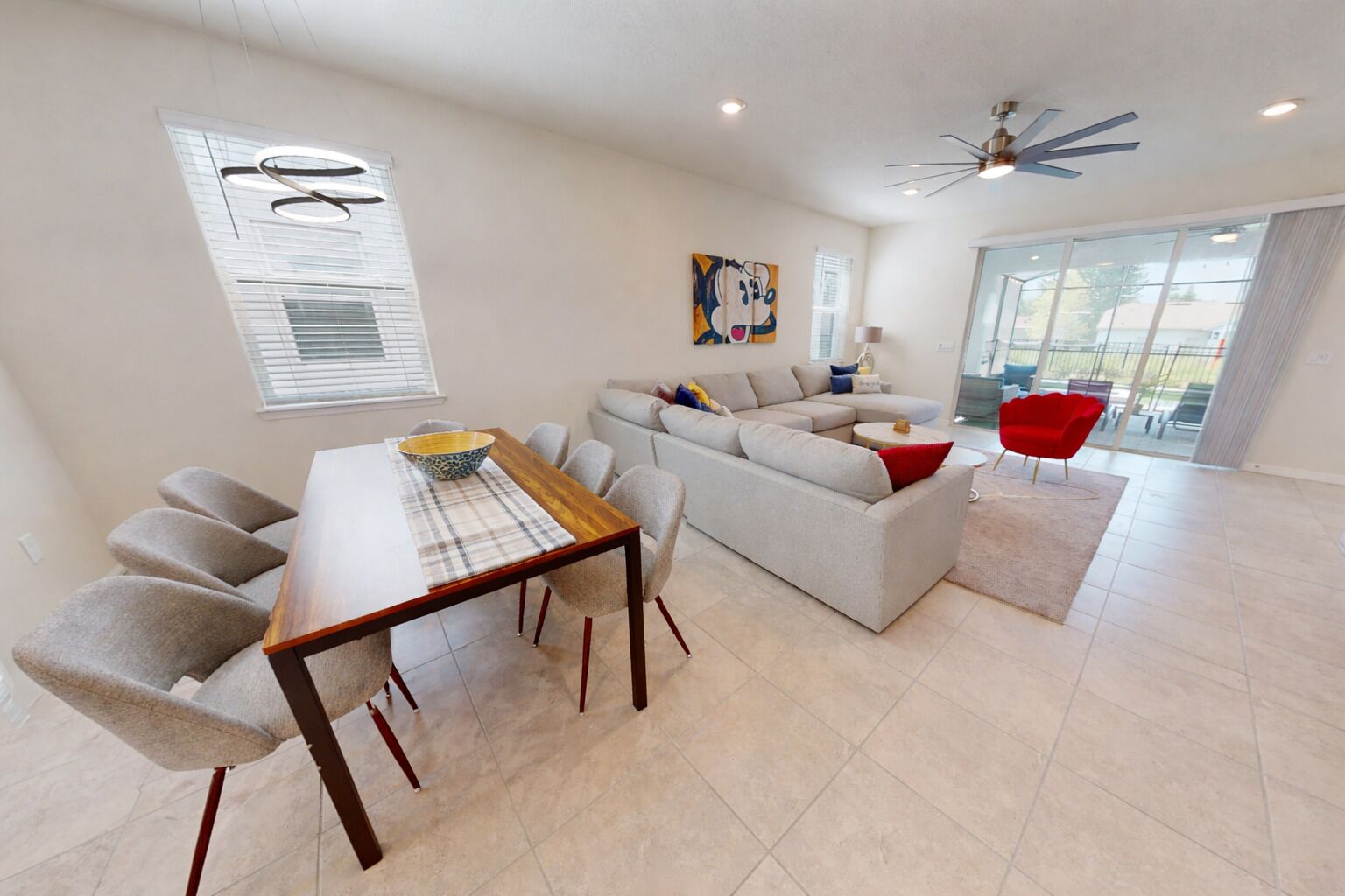 A modern living room with a dining area, a sofa set, a red chair, and a ceiling fan.