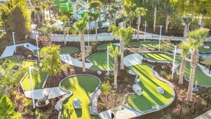 Un campo da golf con diversi putting green, palme e un parco acquatico sullo sfondo.