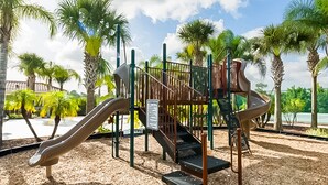 Ein Spielplatz mit Rutschen und Klettergerüsten, umgeben von Palmen und blauem Himmel.