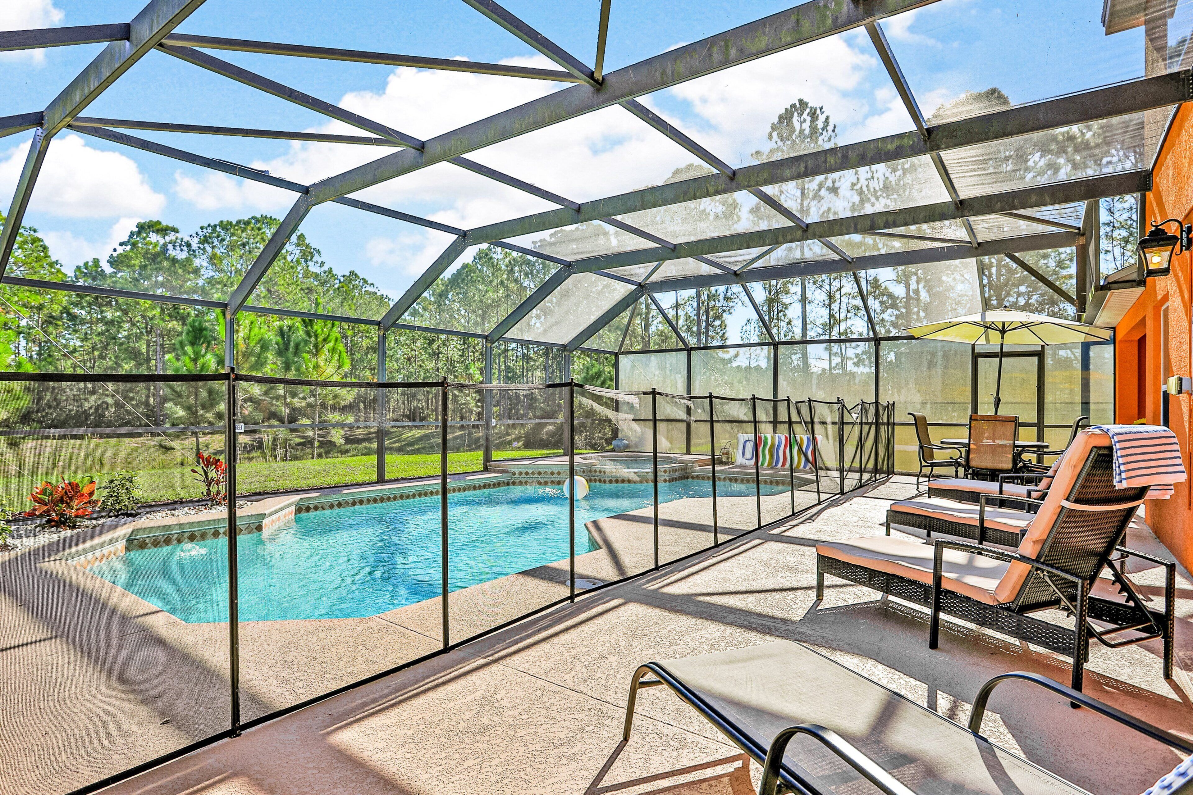 A covered outdoor swimming pool with lounge chairs and a table, surrounded by a metal frame and glass panels.