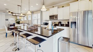 Une cuisine moderne dotée d’un îlot central, d’appareils électroménagers en acier inoxydable et de luminaires suspendus.
