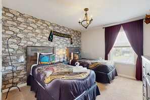 A room with a stone wall, two beds with themed bedding, a chandelier, and a window with curtains. - Spacious Resort Style Home w/ Enclosed Pool, Shared Pool & hot Tub,-dog Friendly (Kissimmee)