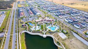 Vue aérienne d’un quartier résidentiel avec un parc central, une piscine et un pont.