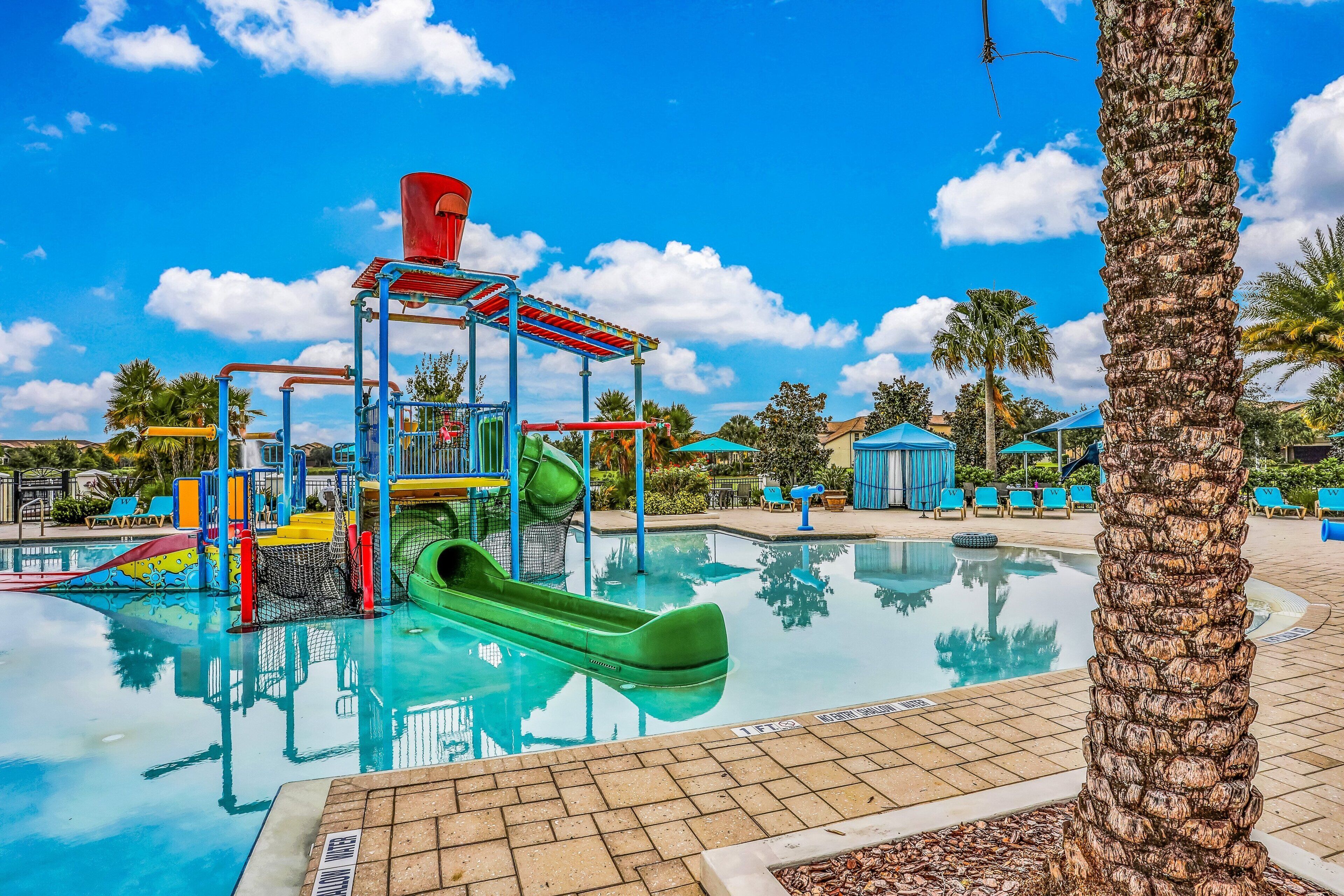 A pool area with a water slide, palm trees, and a clear blue sky.