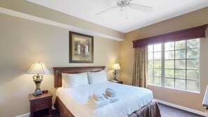 Hotelkamer met een bed, twee bedlampen, een plafondventilator, een raam met gordijnen en een schilderij aan de muur.