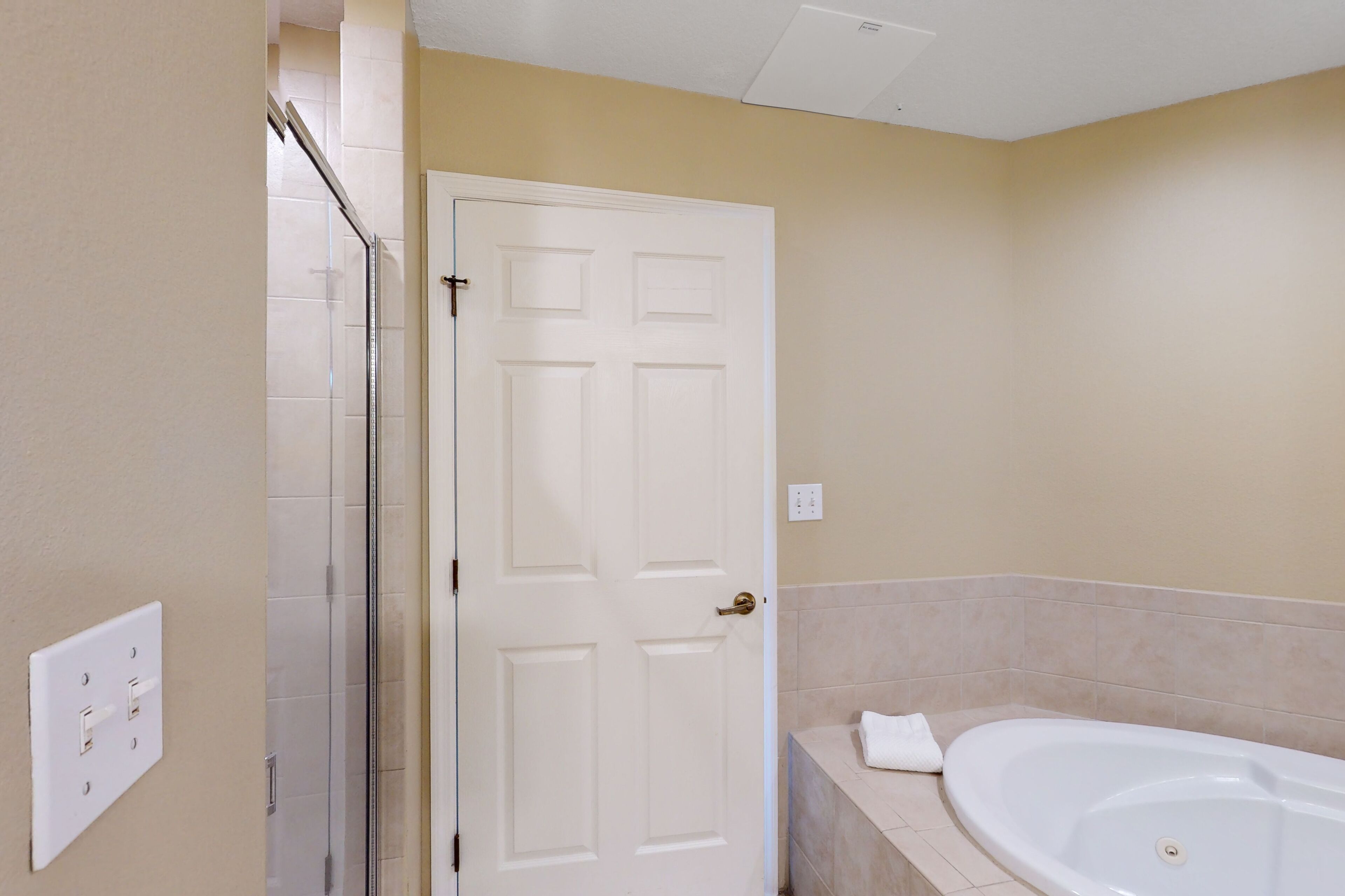 A bathroom with a white bathtub, a glass shower enclosure, and beige walls.