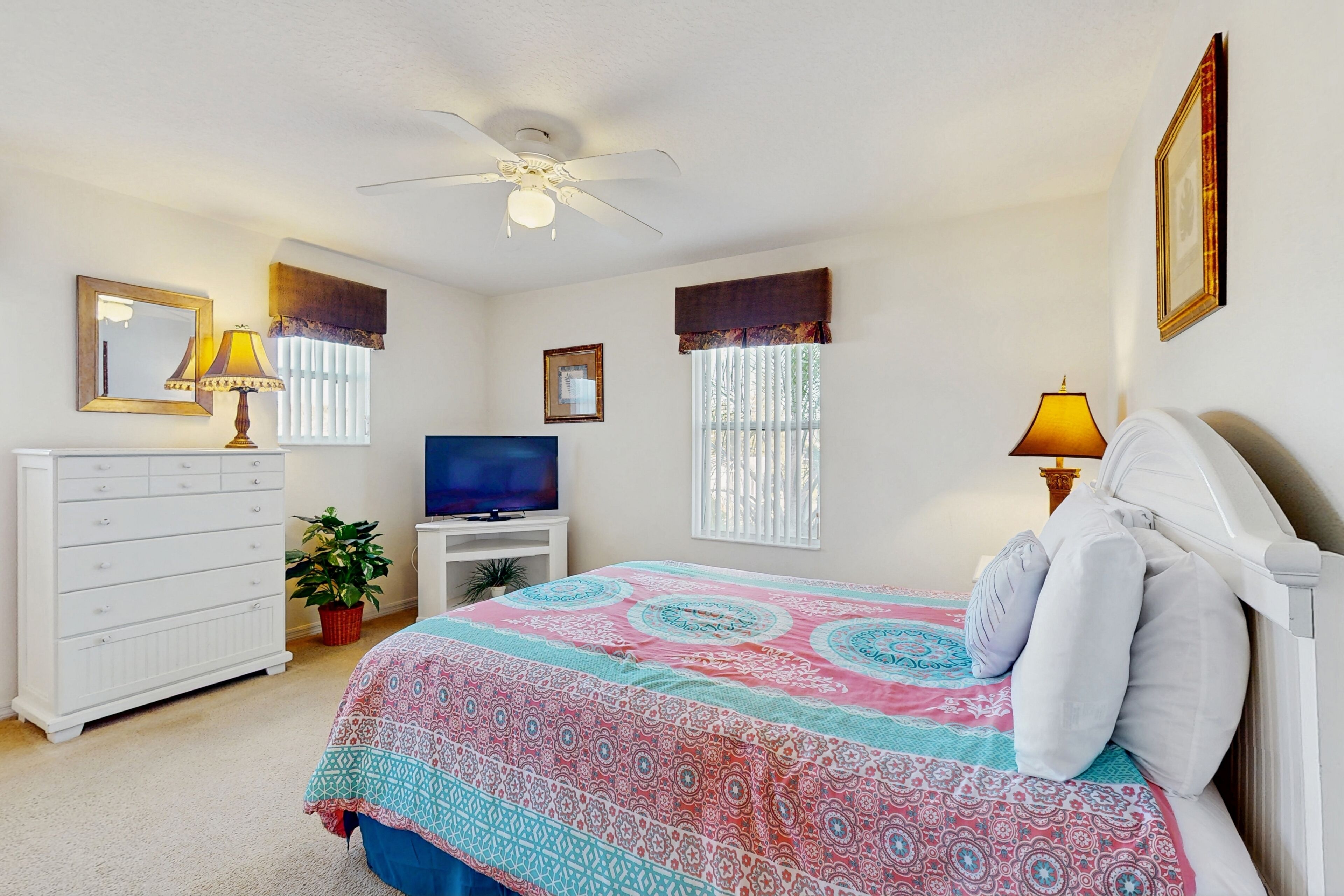 A bedroom with a bed, a dresser, a TV, a ceiling fan, and a window with curtains.