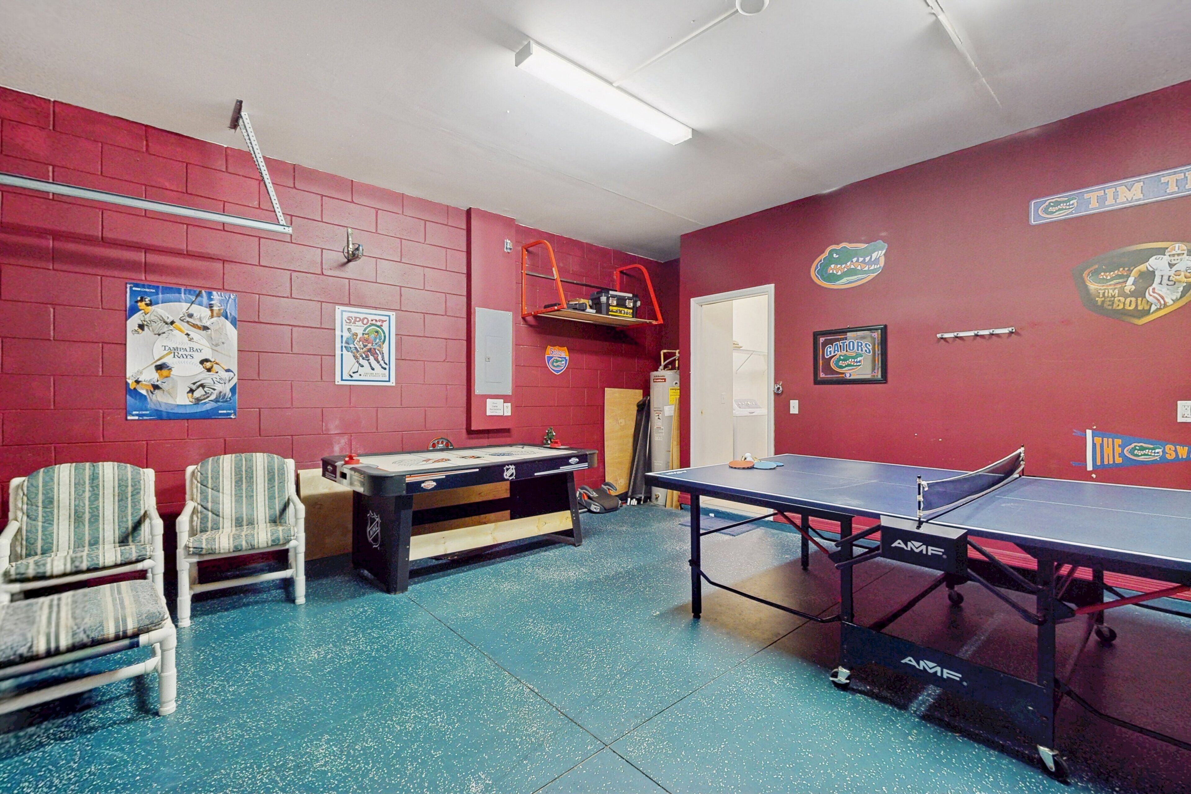 A room with a ping pong table, chairs, a pool table, and sports memorabilia on the walls.